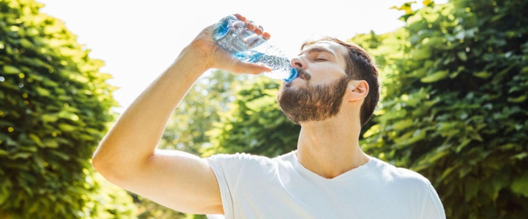 A man in a garden drinking water from a bottle